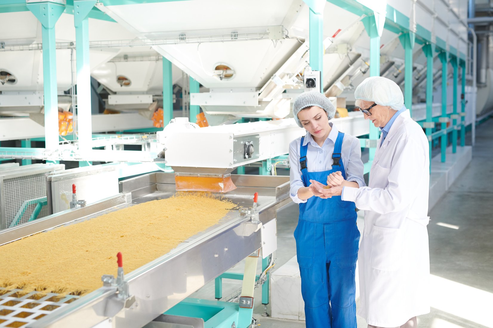 Two individuals in aprons standing in front of a conveyor belt