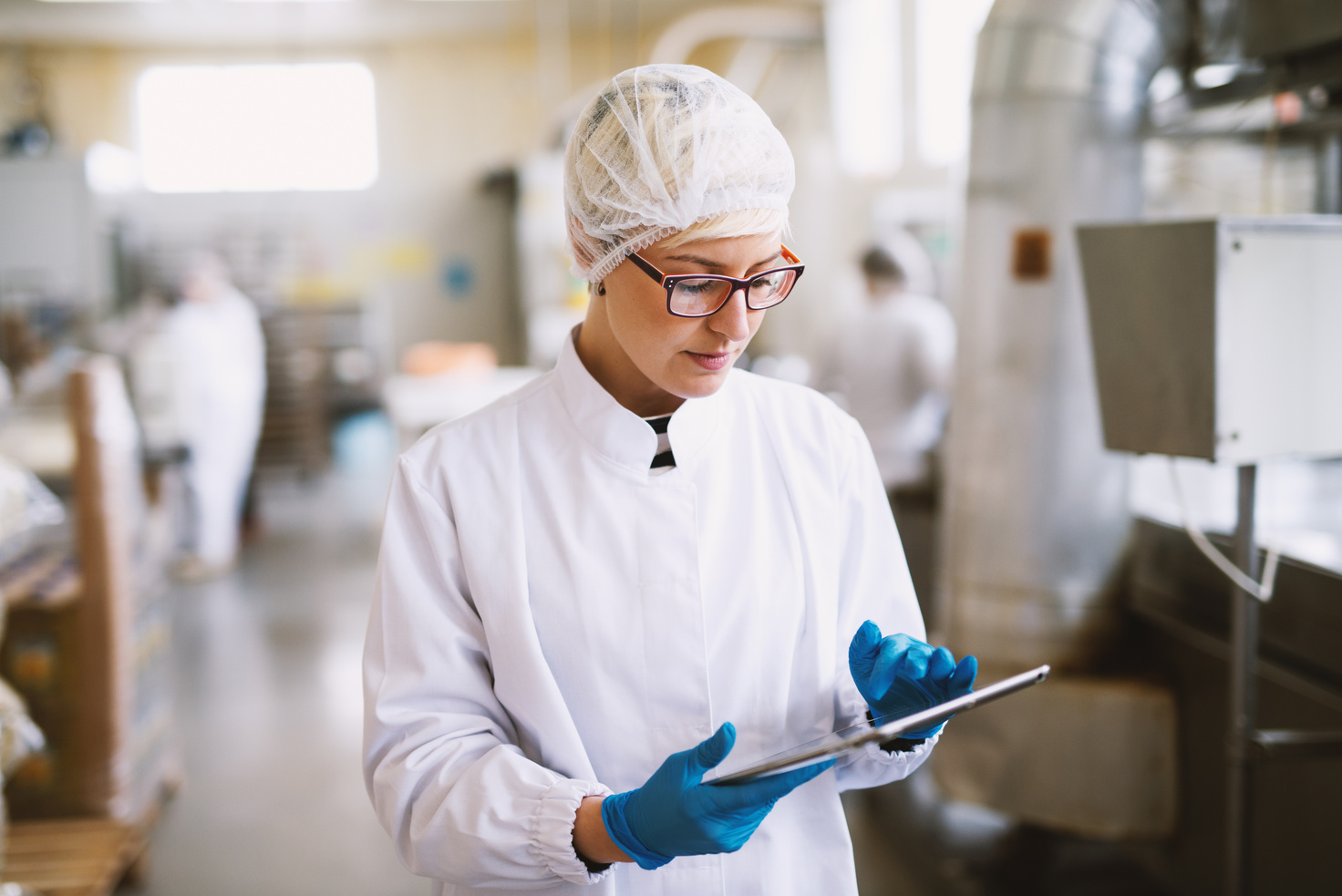 a factory worker in a white lab coat is using a touch screen instrument to collect data relating to food safety controls in the factory