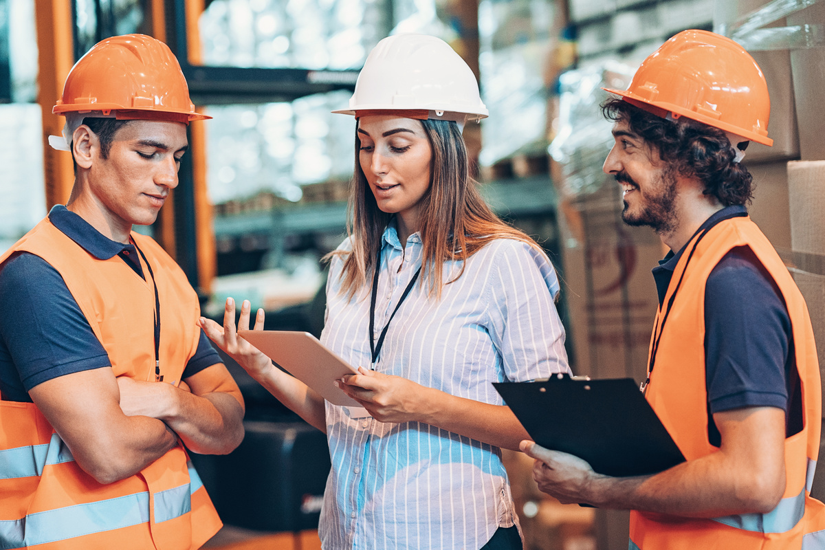 Health & Safety trainer, helping three factory workers who work in warehouse about the importance of health and safety at work.