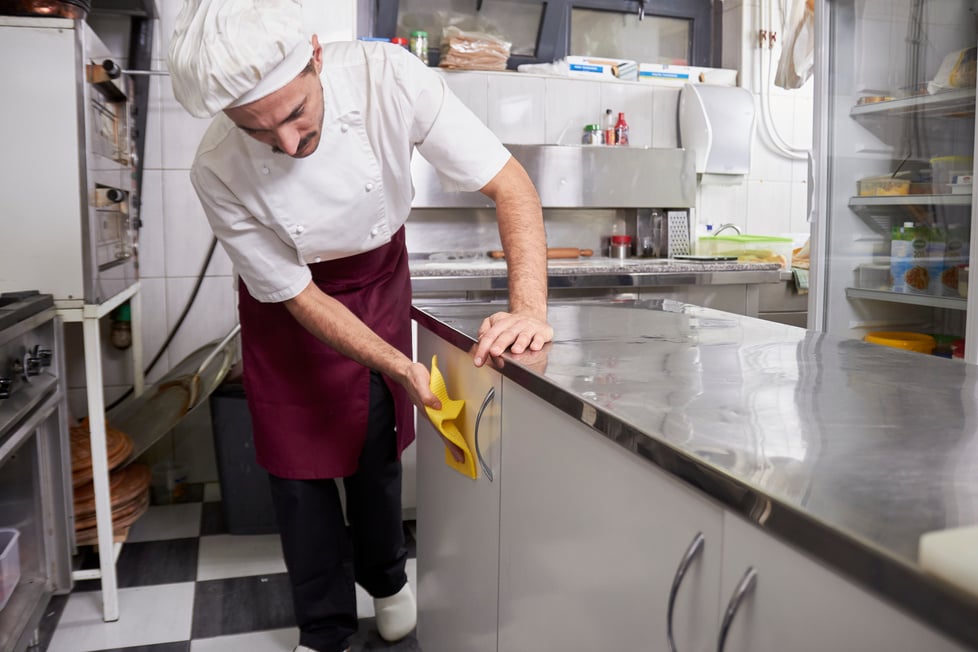 chef/porter/cleaner in an apron cleaning a counter in a kitchen