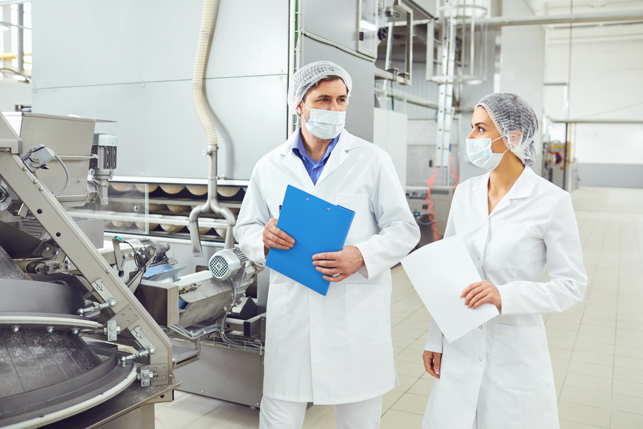 Food Safety auditors in white lab coats standing in front of a machine and making their food safety related observations.