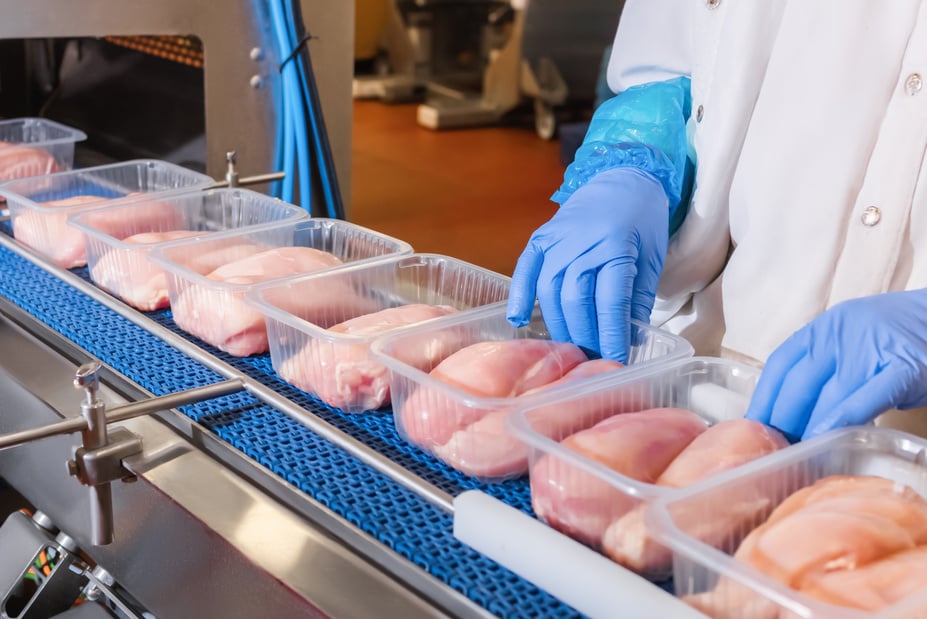 a person in blue gloves and gloves is placing chicken in plastic containers on a conveyor belt in food factory