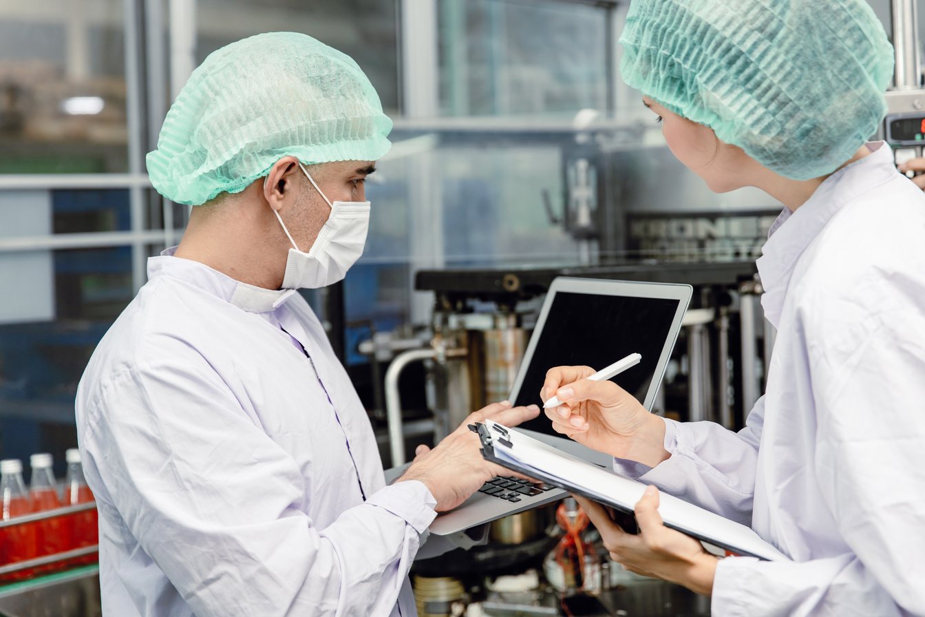 Factory workers in white lab coats being trained at work in a factory 