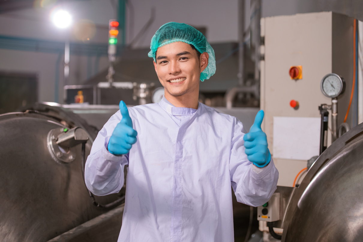 A factory operative in a lab coat giving the thumbs up on the factory floor.