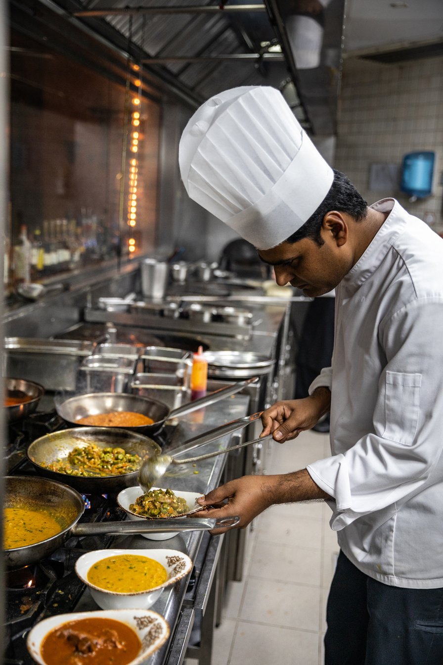 a chef preparing food in a Indian commercial kitchen, he is smartley dress with all PPE