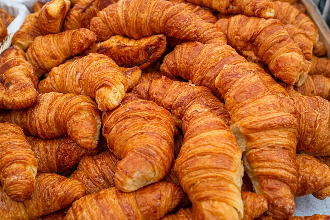 A close up of a freshly baked tray of golden looking crossants for sale at a farmers market